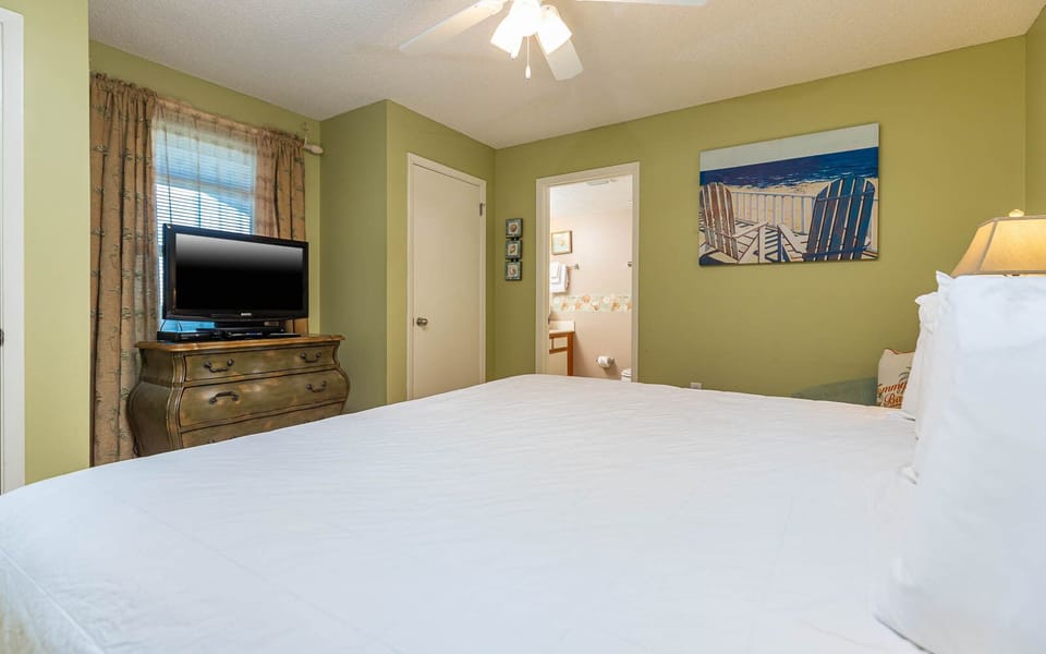 Spacious guest bedroom features a comfortable king bed, a TV on a vintage dresser, and a vibrant beach artwork on the wall
