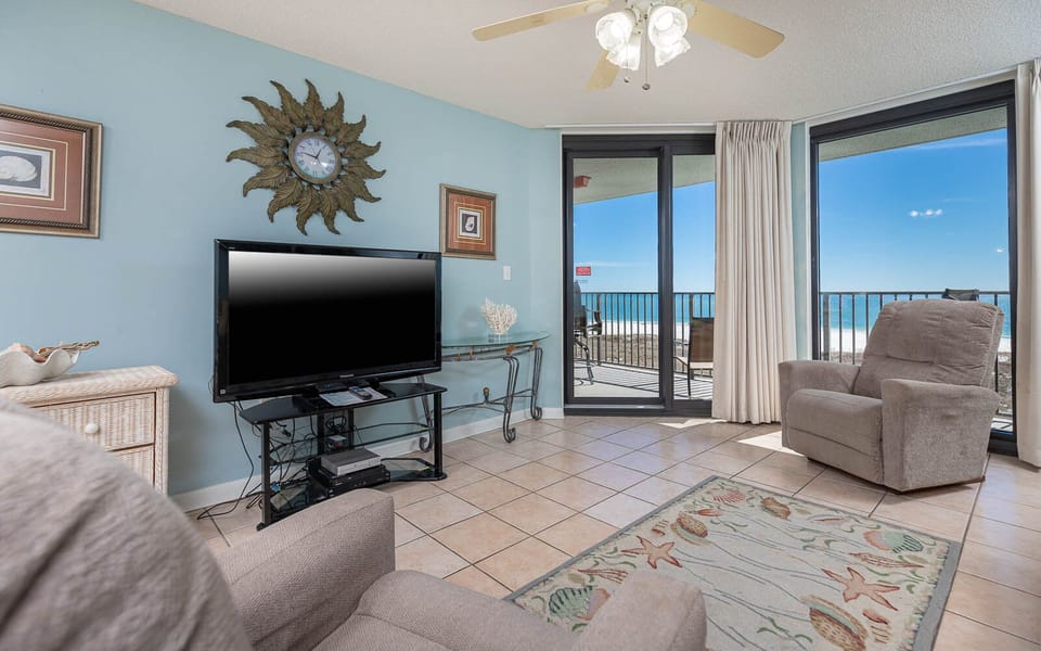 Living area features a large TV, sofa with queen sleeper, and sliding glass doors opening to a balcony with a gulf view