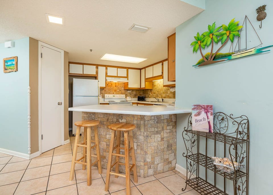 Inviting kitchen area features a breakfast bar with wooden stools, complemented by stone accents and tropical decor