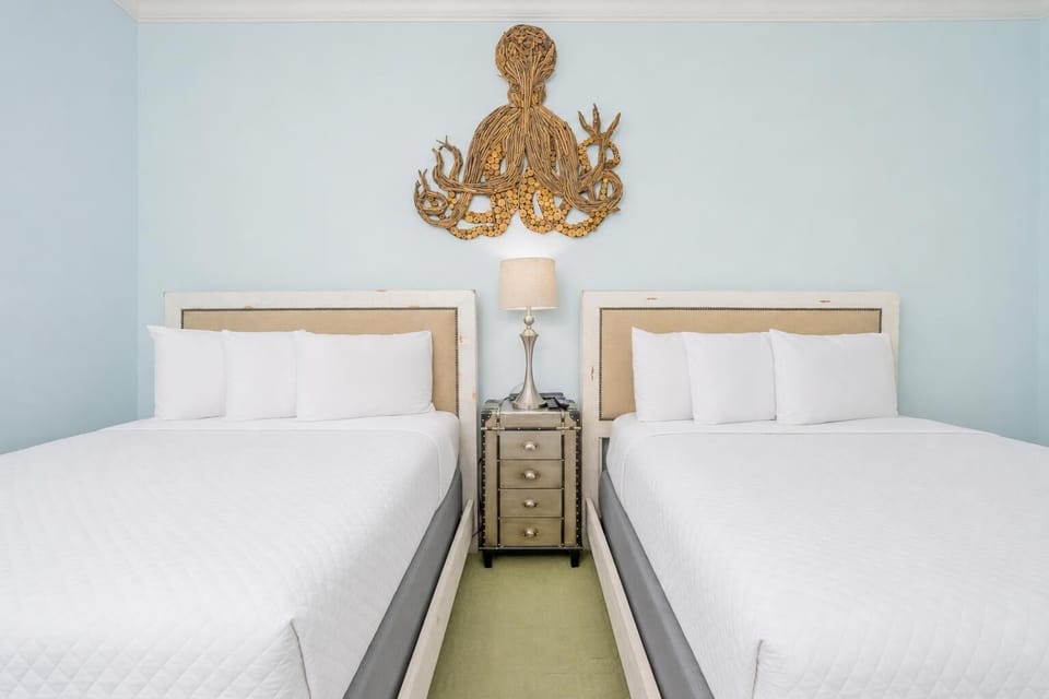 Inviting guest room featuring two queen beds, soft linens, and a charming octopus decor piece above the headboards