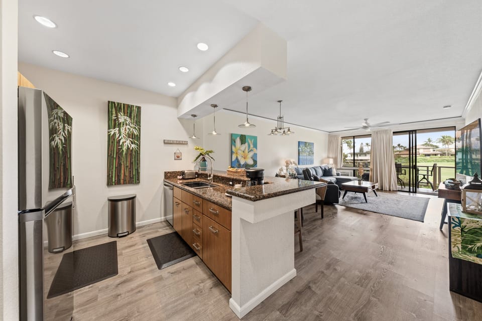 Kitchen joins the flow with wood cabinetry and granite, pendant lights and steel appliances anchoring the open plan.