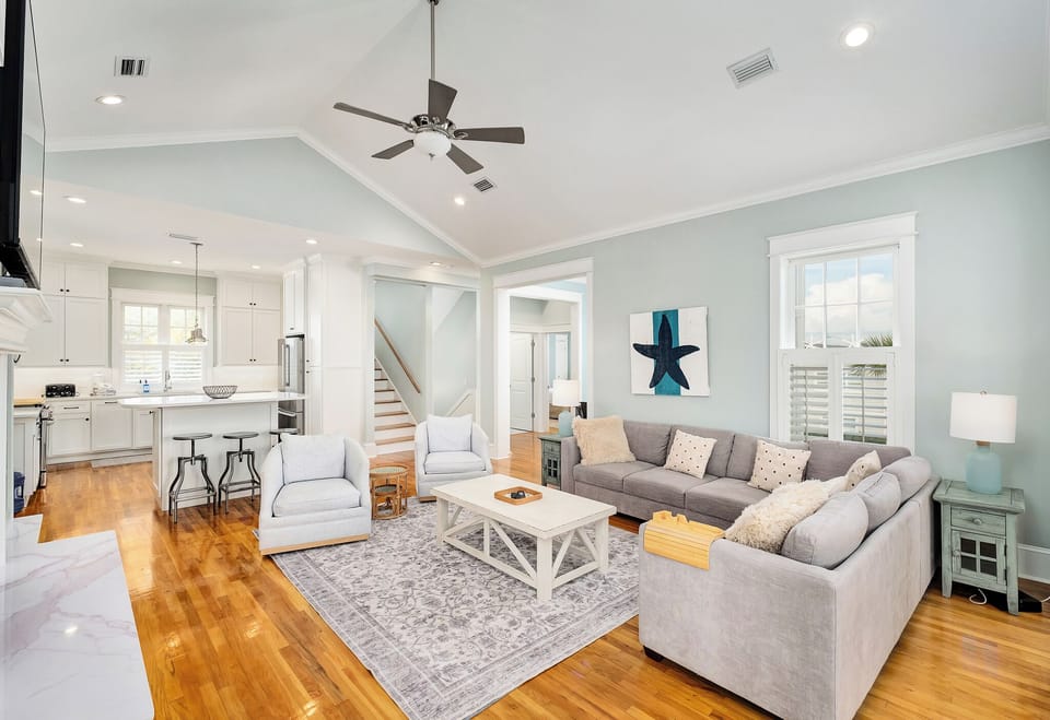 Relax in this bright open-concept living space where coastal colors meet modern comfort, complete with plush sectional seating and gleaming hardwood floors.