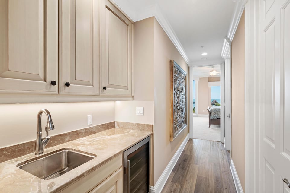 Butler’s pantry with beige cabinetry, marble countertop, stainless steel sink, wine fridge, and carved wood wall art.