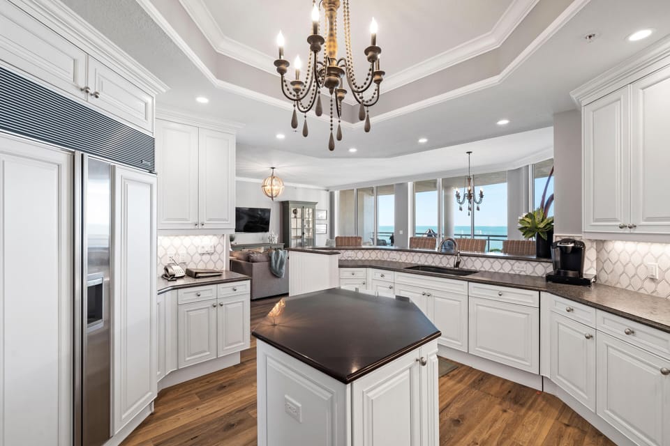 White cabinetry and dark granite countertops surround a hexagonal kitchen island with pendant lighting overhead.
