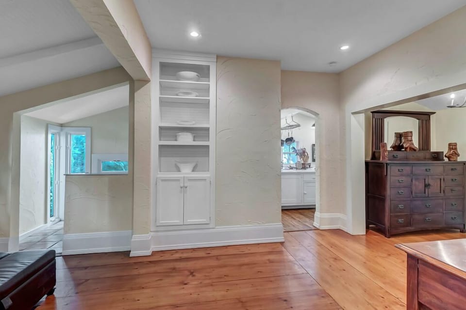 - Hallway features built in shelving, warm toned wood floors, and architectural detail
- Arched entryways lead to the kitchen and other living areas with charm
- Subtle lighting and vintage decor highlight the home's character and flow