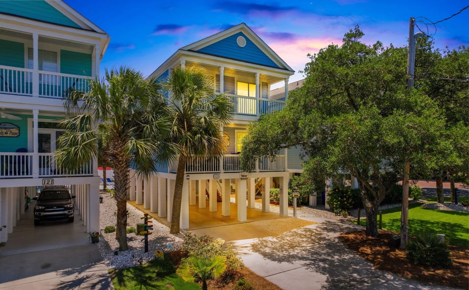 Charming coastal home with tropical palm trees and illuminated evening ambiance in a peaceful residential setting.