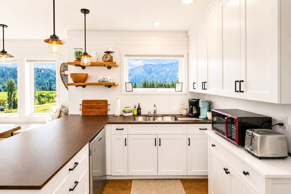 Your bright, farmhouse-style kitchen welcomes you with gleaming white cabinets, warm wood counters, and stunning mountain views through every window—a perfect spot to brew morning coffee.