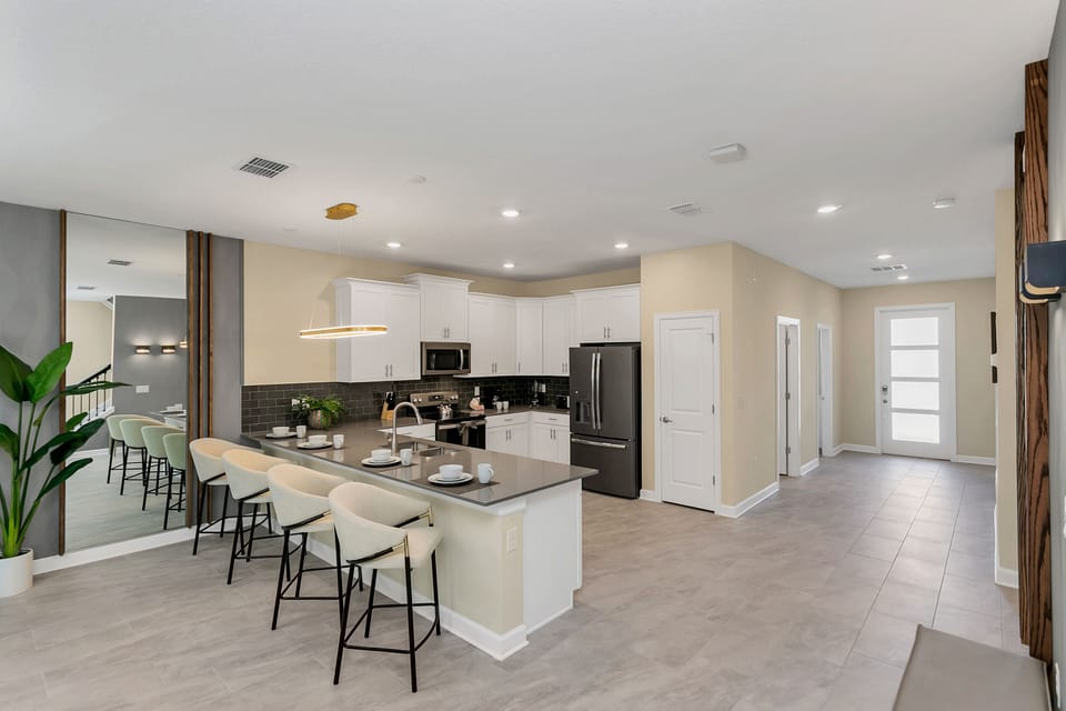Modern kitchen of the home in Kissimmee Florida - Strategic use of mirrors to enhance the perception of space - Breakfast bar and high chairs - Stainless steel appliances - Thoughtful placement of kitchen essentials for easy access
