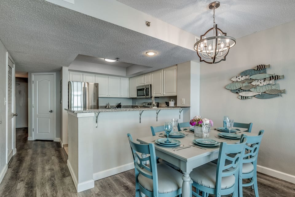 Teal dining set under chandelier next to sleek kitchen with coastal decor