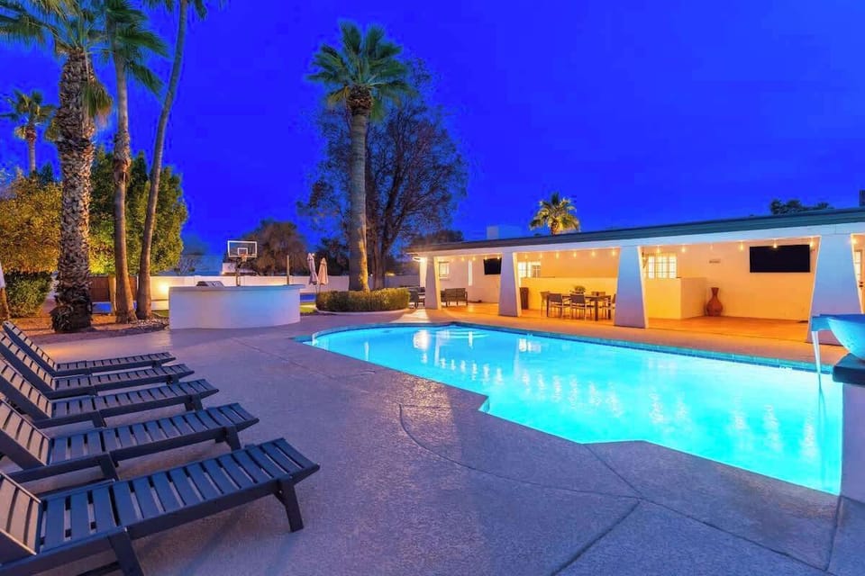 Stunning evening ambiance awaits with a luminous pool, loungers perfectly positioned for relaxation, and an open-air dining space glowing warmly under swaying palms.