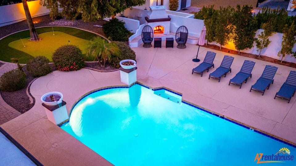 Luxurious backyard oasis featuring a sparkling pool, modern outdoor fireplace, and lounge chairs for ultimate relaxation under evening lights.