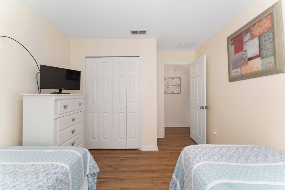 This cozy bedroom offers two twin beds adorned with light blue linens and warm wood flooring for comfort. A contemporary dresser provides storage, and a wall-mounted TV invites you to relax after your day of adventure.
