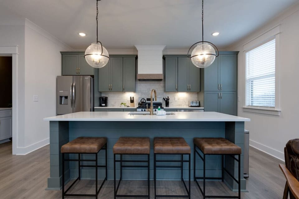 Modern kitchen with dark teal cabinetry, marble island, bar stools, and pendant lights