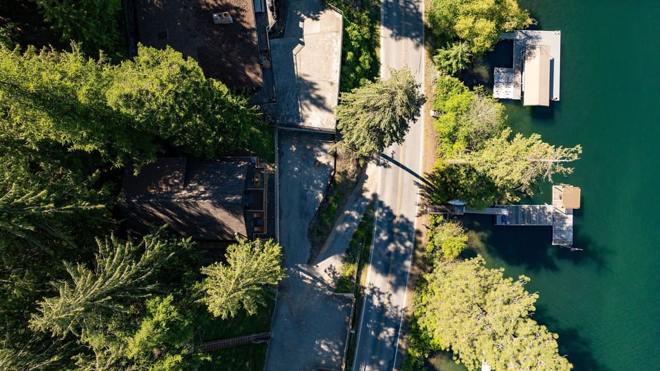 Aerial perspective of waterfront properties nestled along a tranquil green lake, surrounded by mature trees and private docks, showcasing the serene natural setting.