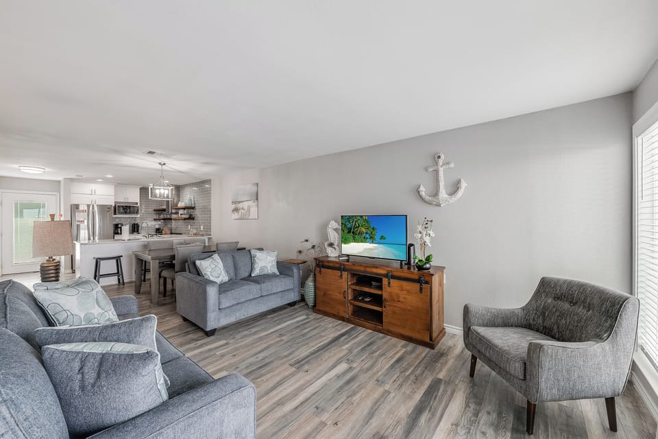 Sink into plush gray sofas in your open-concept living space, where coastal charm meets modern comfort with stylish nautical touches and entertainment center.