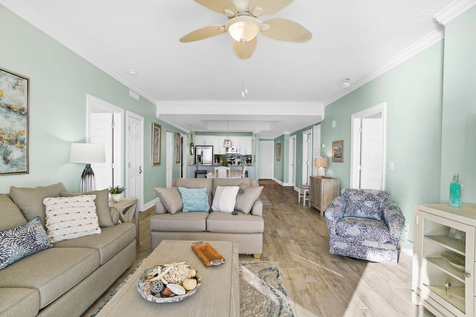 Relax in your spacious living room with calming mint walls, coastal décor, and a gentle ceiling fan creating the perfect beachy retreat.