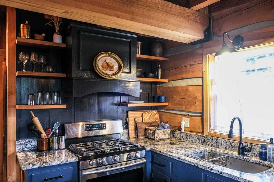 Designer renovated kitchen featuring custom hood vent, granite countertops, hardwood floating shelves, & gas range.
