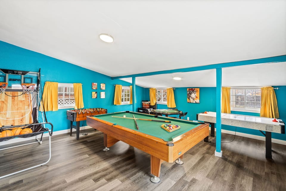 Game On Central! 🎮🌟🏡 - A fully equipped game room featuring a pool table, foosball, poker table, and basketball setup for a diverse and thrilling leisure experience.