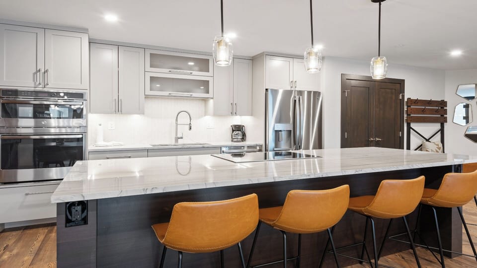 Your modern kitchen invites you to gather around the spacious marble island, where sleek pendant lights cast a warm glow over stainless steel appliances and crisp white cabinetry, ready for your culinary adventures.