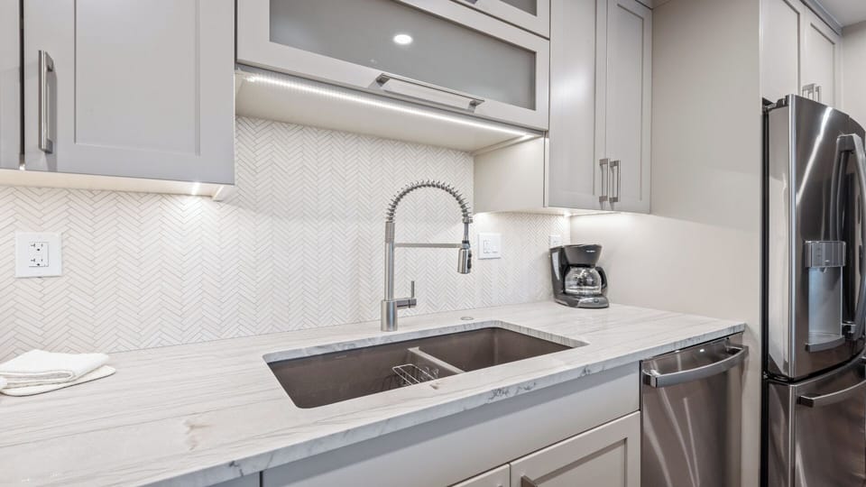 A gleaming kitchen awaits you with polished counters, stainless steel appliances, and elegant herringbone tile backsplash—everything ready for your morning coffee or a leisurely meal.