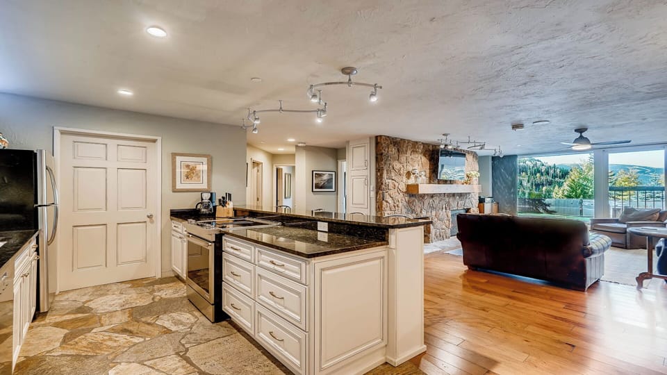 Your open-concept space flows effortlessly from kitchen to living area, where mountain views greet you through floor-to-ceiling windows and warm wood floors invite you to unwind.