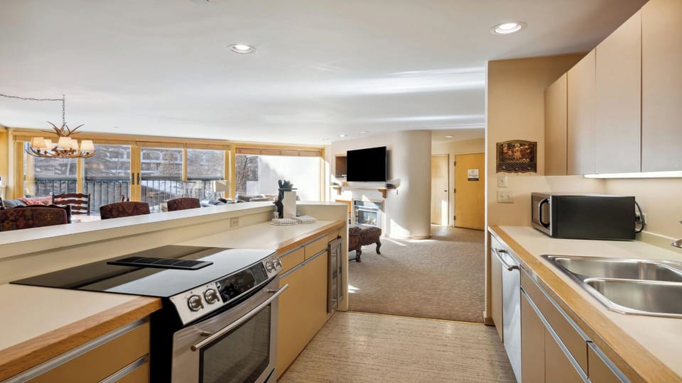 Your open-concept retreat blends a fully-equipped kitchen with a cozy living space, where sunlight pours through large windows to frame wintry views perfect for après-ski unwinding.