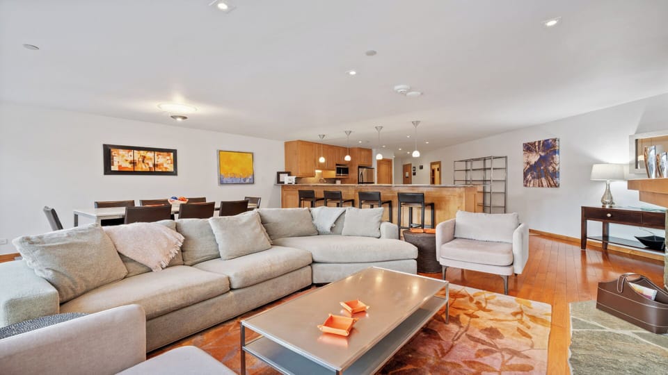 Settle into plush seating in your spacious open-plan living area, where warm wood tones, modern art, and a fully-equipped kitchen create the perfect setting for your getaway.