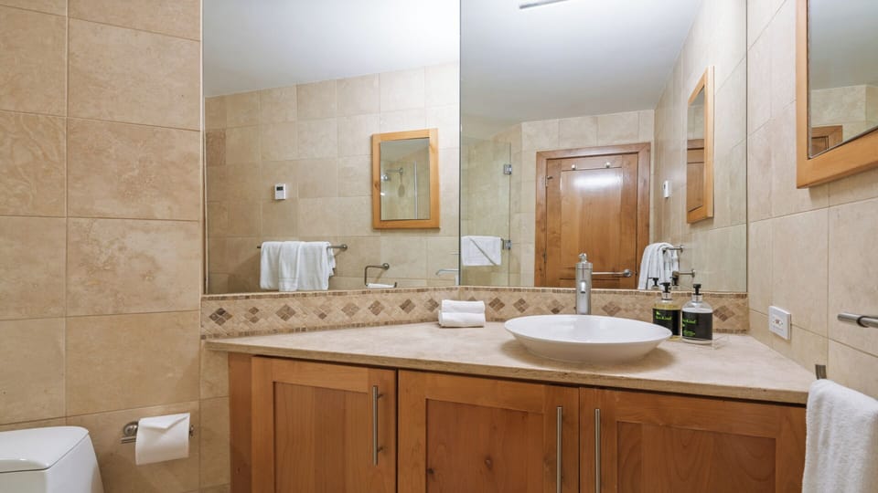 Step into your private spa-like retreat with warm stone tiling, sleek vanity, and plush towels ready for your refreshing morning routine.