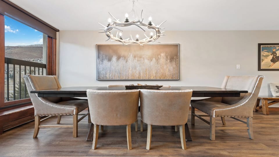 Gather around this elegant dining table where rustic charm meets mountain sophistication. The antler chandelier and landscape art set the tone for memorable meals with your group.