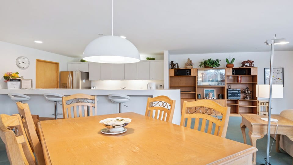 An inviting open-concept space with a warm wooden dining table where you can gather for meals, and a modern kitchen with a bright breakfast bar for casual moments together.