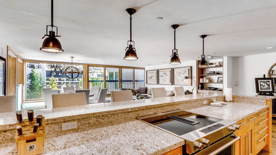 Step into your gourmet kitchen where granite countertops gleam under industrial pendant lights. Cook and entertain with ease as natural light floods through expansive windows, framing your cozy living space beyond.