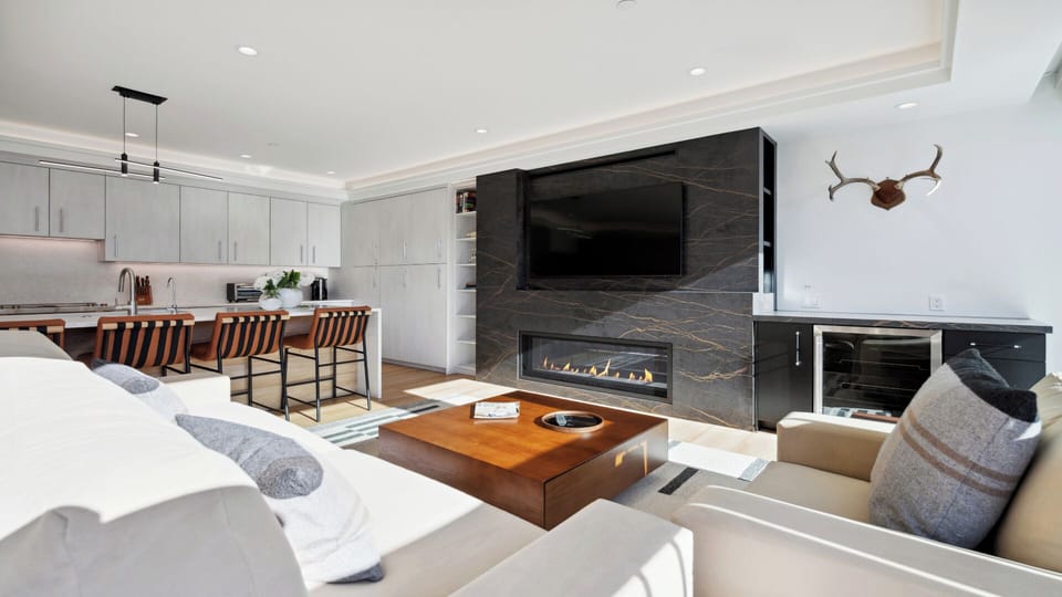Settle into your open-concept retreat where a striking stone fireplace anchors the living space, modern barstools line the kitchen island, and natural light highlights every sleek surface.