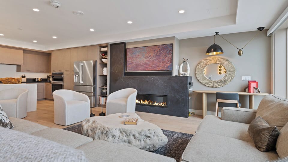 Relax in your spacious living area featuring a sleek modern fireplace, elegant artwork, and plush seating. The open layout connects effortlessly to a gourmet kitchen—perfect for your stay.