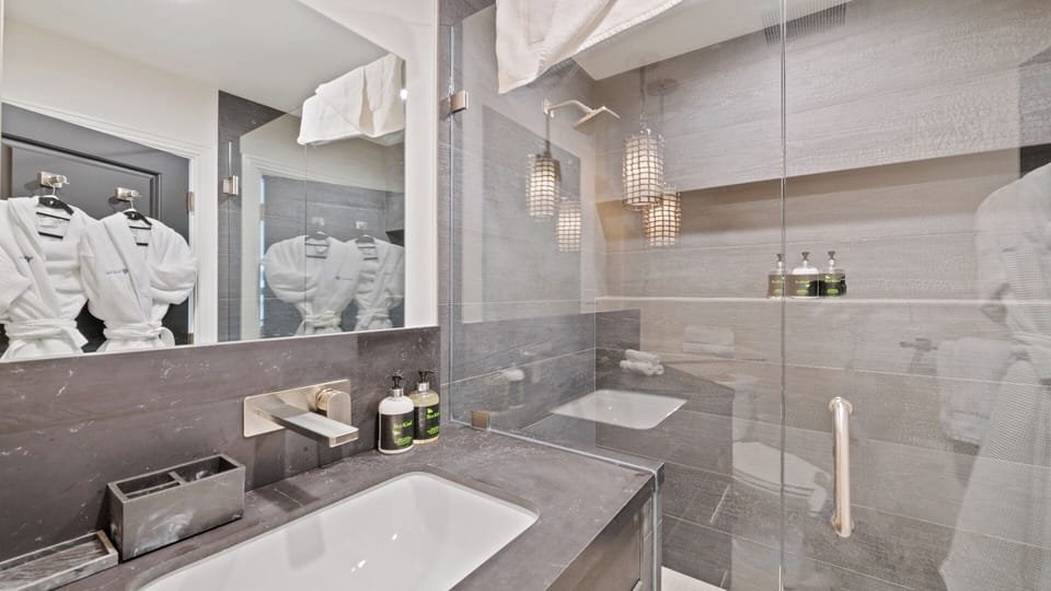 Step into your modern spa-like bathroom, where sleek gray tones, elegant pendant lighting, and plush robes await to make your stay feel effortlessly luxurious.
