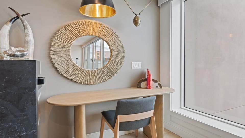A stylish workspace awaits with a modern desk, statement mirror, and elegant lighting to inspire your creativity.