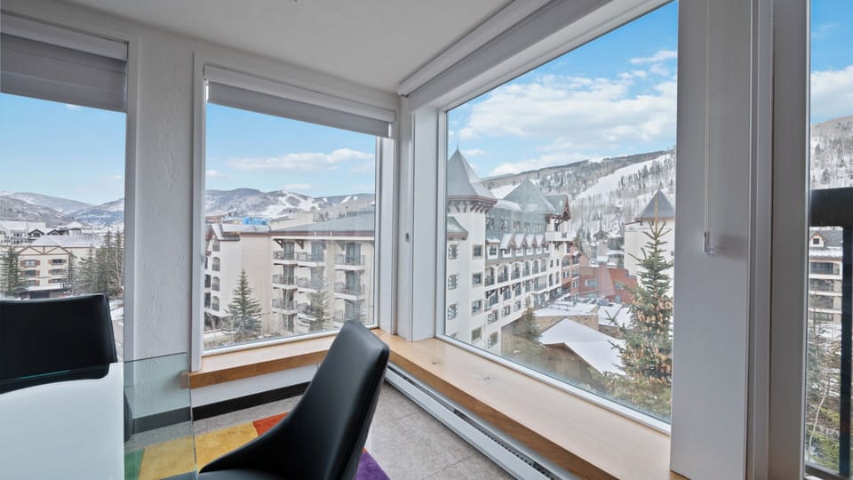 Bright mountain resort views frame this cozy corner workspace, overlooking snow-dusted peaks and alpine architecture—perfect for balancing productivity with panoramic scenery.