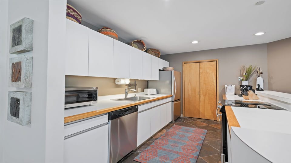 Your fully-equipped kitchen blends sleek white cabinetry with warm wood accents, featuring stainless appliances, ample counter space, and charming basket décor—perfect for whipping up meals or morning coffee.