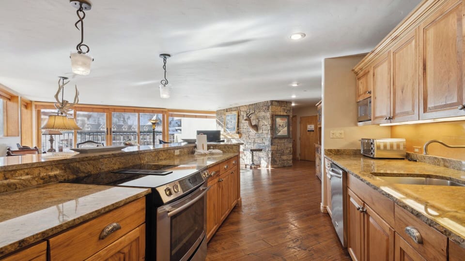 Discover your culinary haven with gleaming granite countertops, warm wood cabinetry, and stainless appliances—plus a cozy stone fireplace setting the scene for memorable mountain meals.