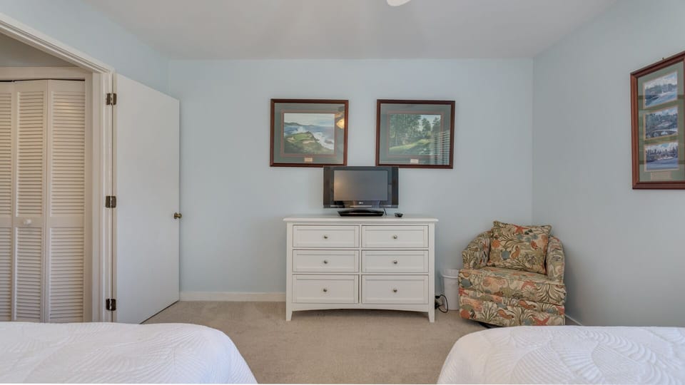 A flat-screen TV, generous dresser storage, and a comfortable reading chair create a relaxed, functional space.