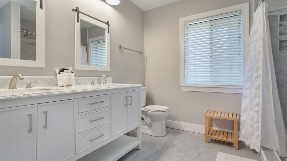 Neutral finishes, a bright window with blinds, and crisp white vanity with ample storage create a light, spa-inspired space that's both practical and inviting.
