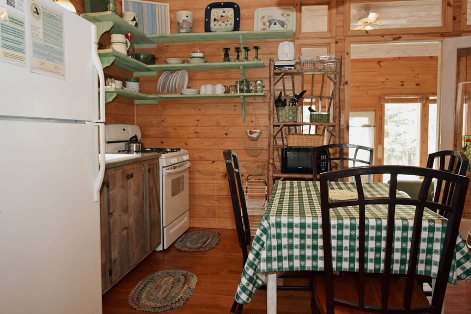 Your cozy cabin kitchen awaits with rustic wood walls, open shelving stocked with essentials, and a dining table ready for shared meals and morning coffee.