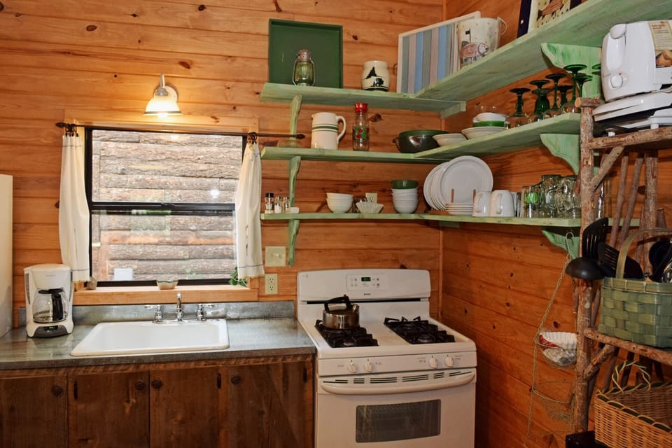 Step into your rustic retreat where open shelving displays charming dishware and a cozy window over the sink frames peaceful woodland views beyond.
