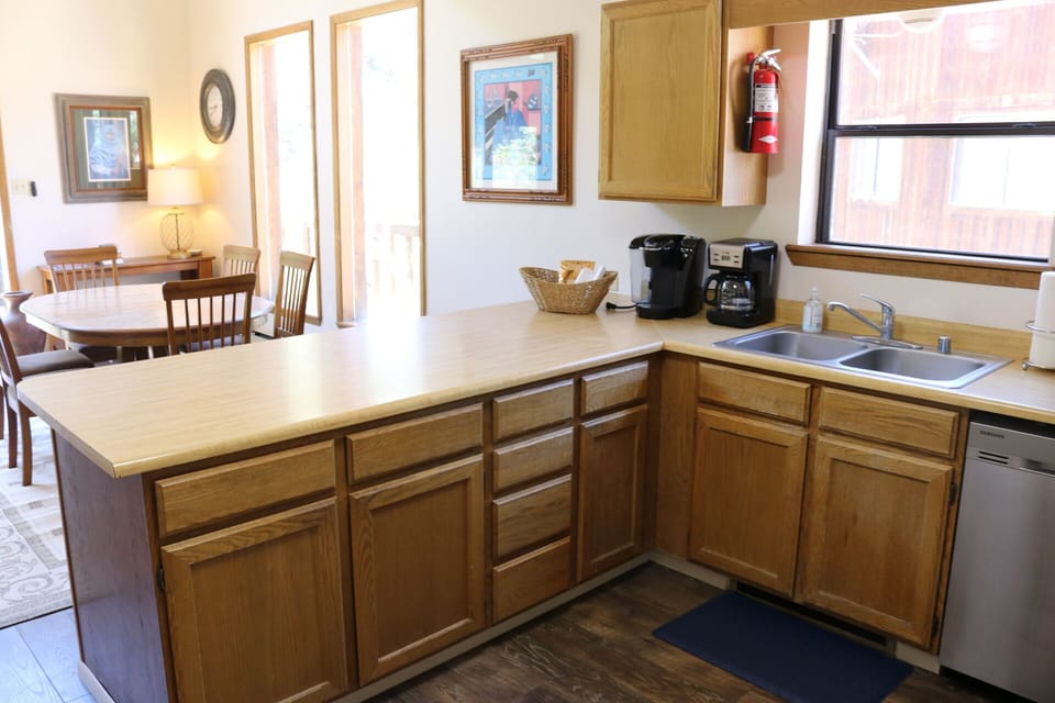 Your fully equipped kitchen with warm wood cabinets, double sink, dishwasher, and coffee makers makes meal prep easy while you enjoy natural light and charming artwork on the walls.