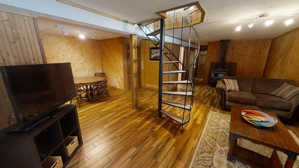 Unwind in your cozy living space featuring warm wood finishes, comfortable seating, and a spiral staircase leading to the loft—perfect for relaxing after a day of adventure.