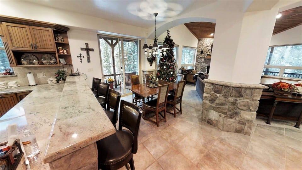 Gather around the elegant dining table for memorable meals, with natural light streaming through doors that open to scenic winter views and a cozy stone bar nearby.