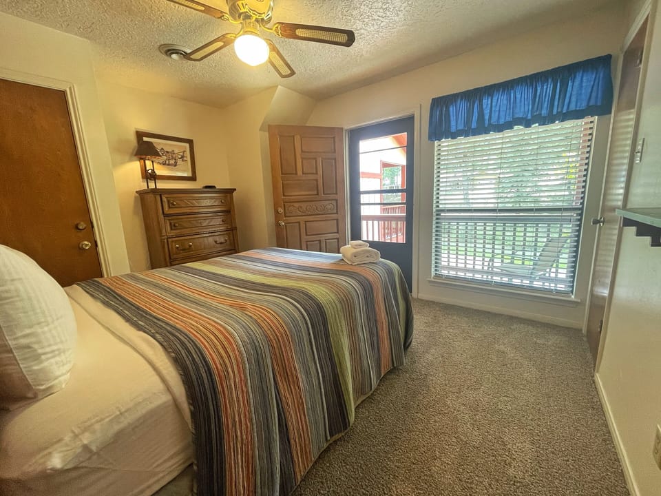 Sink into your comfy bed with colorful striped linens, where a ceiling fan keeps you cool and a cozy window lets in natural light. Fresh towels and warm wood furnishings make this space feel like home.