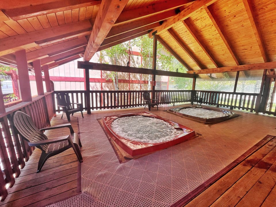 Unwind on your private covered deck with vaulted wood ceilings, comfortable seating, and twin hot tubs framed by garden views—perfect for relaxing outdoors in any weather.