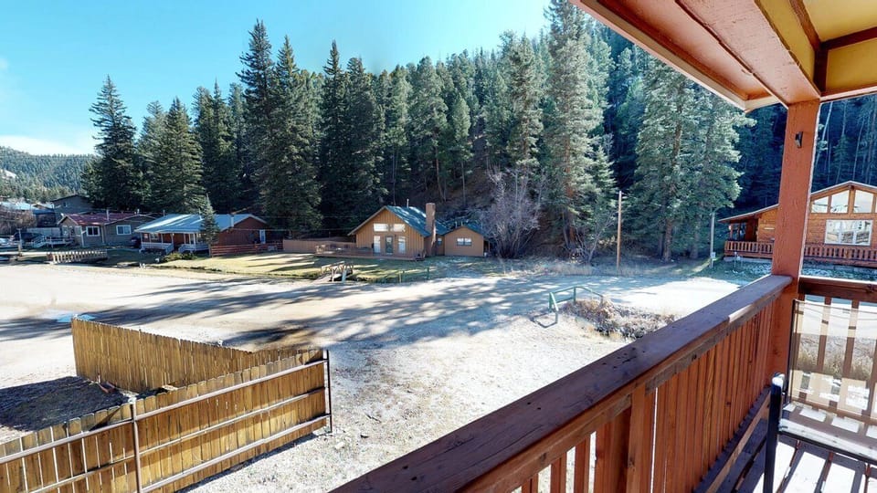 The property is nestled in a mountain area with forested hillsides, neighboring cabins, and a shared community yard visible in the crisp winter season.