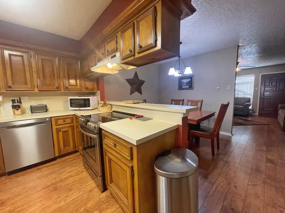 Your fully equipped kitchen flows seamlessly into the dining area, offering warm wood cabinetry, modern stainless appliances, and a central island—perfect for gathering and cooking during your stay.