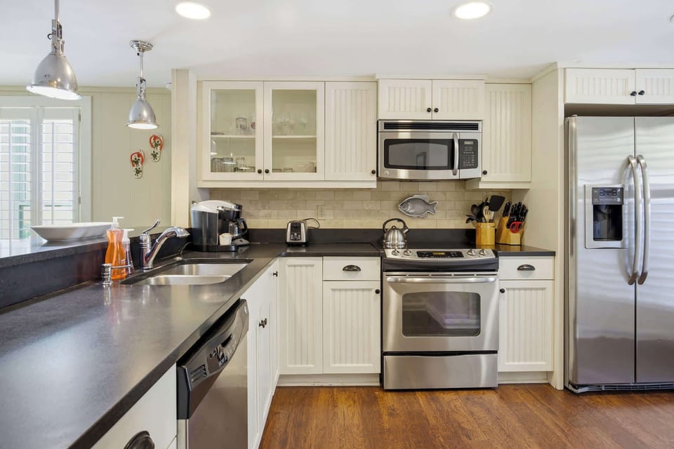 Creamy beadboard cabinetry and dark, expansive counters create a classic, coastal atmosphere for your morning coffee. Polished stainless appliances and rich wood floors anchor this bright, fully equipped space where every meal feels like a breeze.
